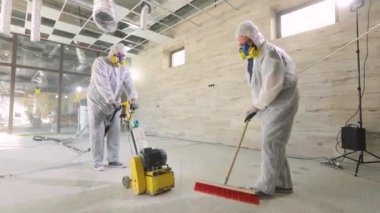 İnşaat işçileri. İnşaat alanında çalışma süreci. Koruyucu giysiler içindeki işçiler beton zemini öğütüyor. İşçiler beton döşeme yapıyor