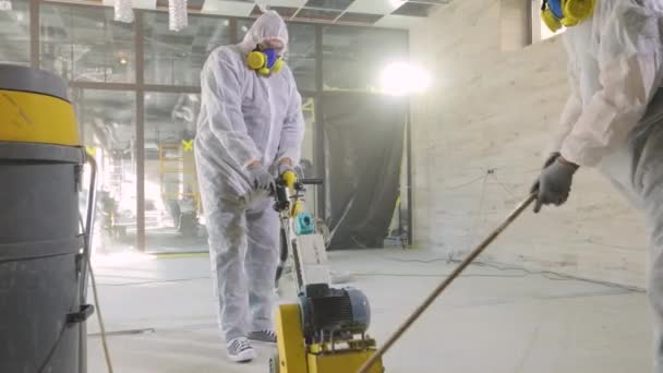 Budowniczowie polerują podłogę specjalnym wyposażeniem. Szlifowanie powierzchni betonu. Budowniczowie na placu budowy — Wideo stockowe