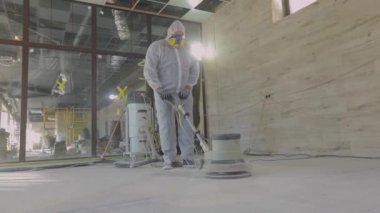 İnşaat alanında çalışma süreci. Koruyucu giysiler içindeki işçiler beton zemini öğütüyor. İnşaat işçileri. İşçiler beton döşeme yapıyor