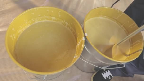 A mexer tinta num balde. Um close-up de tinta amarela sendo mexido em um balde — Vídeo de Stock