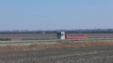 Kırmızı römorklu bir kamyon otoyol boyunca gidiyor. Kamyon yol boyunca gidiyor. Kamyonla mal teslimatı.