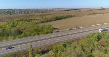 Kamyon, tarımsal alanların ortasında yol boyunca gidiyor. Kamyon yolda, tarlalar arka planda.