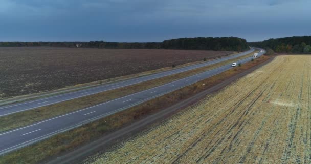 Lastbilar färdas på en rak väg vid solnedgången ovanifrån. Lastbilar kör längs motorvägen bland fälten vid solnedgången. — Stockvideo