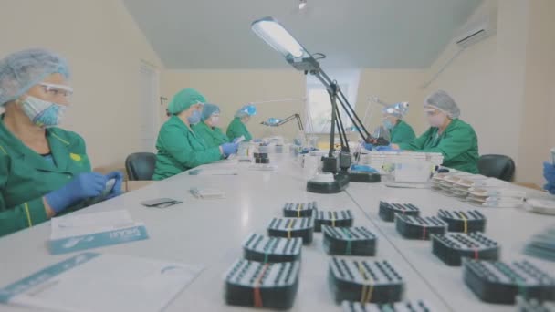 Maskerade arbetare. Fabriksarbetare packar tablettblåsor i kartonger. Förpackning av piller i en fabrik. — Stockvideo