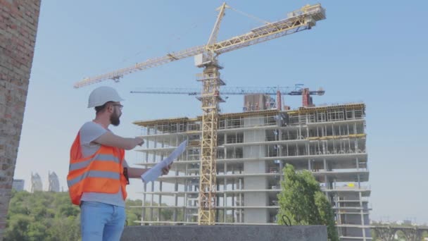 Ein Ingenieur mit einer Zeichnung auf einer Baustelle. Jungingenieur auf einer Baustelle. Ingenieur auf einer Baustelle — Stockvideo