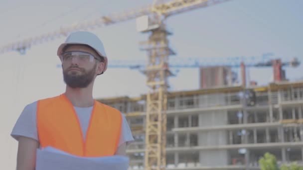 Ingeniero en una obra de construcción. Ingeniero joven en una obra de construcción. Un ingeniero con un dibujo en una obra de construcción. — Vídeos de Stock