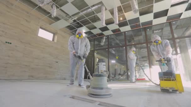 Los trabajadores en trajes de protección están moliendo el suelo de hormigón. Proceso de trabajo en una obra. Profesionales de construcción. Los trabajadores hacen piso de hormigón — Vídeos de Stock