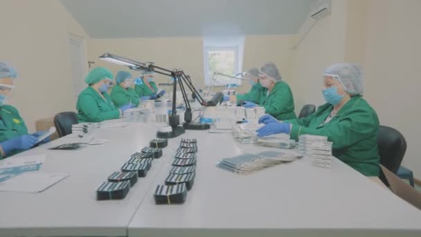 Masked workers. Factory workers pack blisters of pills into boxes. Packaging of pills in a factory. — Stock Video