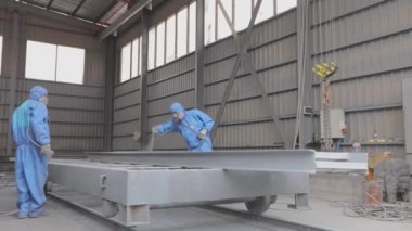 İki işçi bir fabrikadaki boya kutusuna metal bir kiriş çiziyor. Boyama parçaları