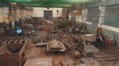 Metal yapıların montajı için bir fabrika. Metal montaj atölyesinde kaynakçı. Metal yapıların montajı için atölye boyunca bir açıklık.