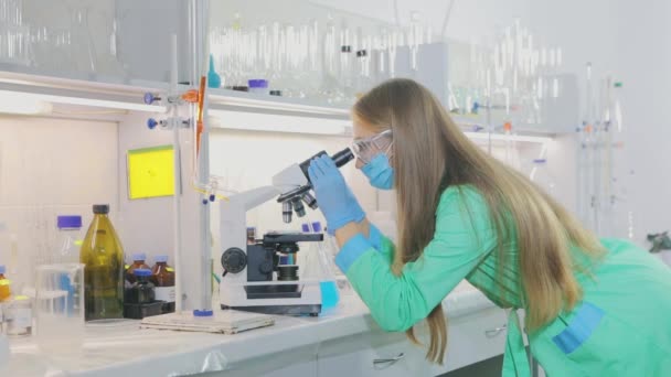 Kız mikroskopla yakından bakıyor. Bilim adamı bir laboratuarda mikroskoba bakıyor. — Stok video