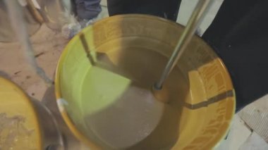 Kovada boya karıştırmak. Yakın plan sarı boya kovada karıştırılıyor.