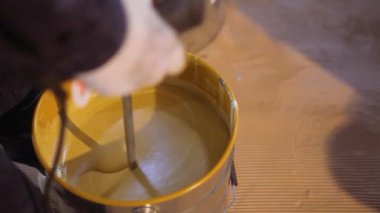 Kovada boya karıştırmak. Yakın plan sarı boya kovada karıştırılıyor.