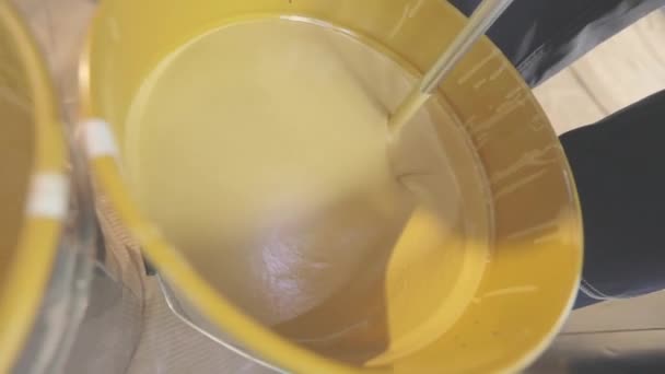 Egy közeli sárga festék keveredik egy vödörben. Festékkeverés egy vödörben. — Stock videók