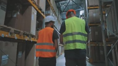 Depodan iki kişi geçiyor. İki adam modern bir depoda yürür ve konuşur.