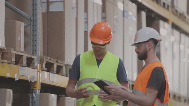 Dois trabalhadores num armazém estão a discutir o trabalho. Engenheiros em um armazém de fábrica — Vídeo de Stock