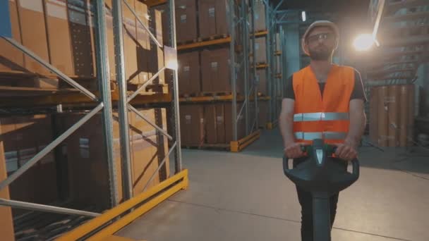 Een werknemer vervoert vracht door het magazijn. Een arbeider loopt door het magazijn met een elektrische hydraulische heftruck. — Stockvideo