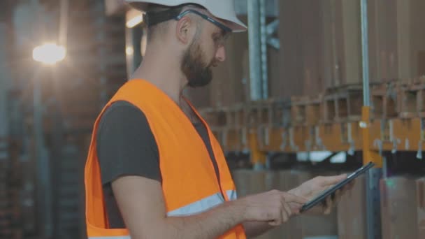 En man i ett modernt lager. Lagerchefen inspekterar lagret. Arbetare i hjälm i ett lager — Stockvideo