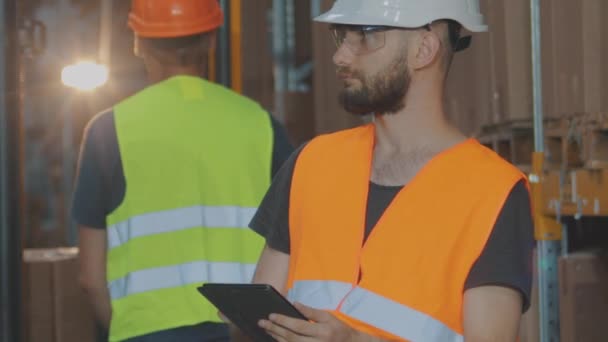 Actief werk in een magazijn. Het magazijn van een moderne fabriek. een magazijnmedewerker in een helm inspecteert de goederen — Stockvideo