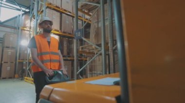 Bir işçi hidrolik forkliftle kutu taşır. Depoda çalışma süreci. Depoda mal taşıyan bir adam.