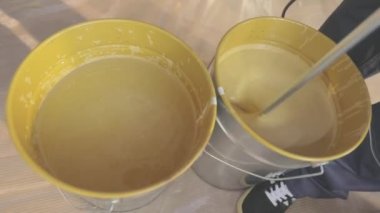 Kovada boya karıştırmak. Yakın plan sarı boya kovada karıştırılıyor.