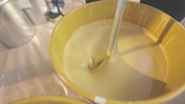 Festékkeverés egy vödörben. Egy közeli kép a sárga festékről, amit egy vödörben kevernek. — Stock videók
