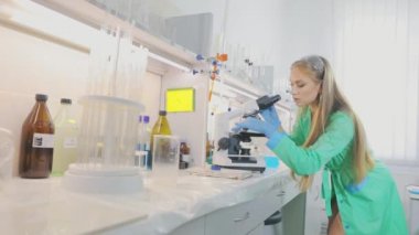 Araştırmacı kız mikroskoba bakıyor. Genç virüs uzmanı kız mikroskoptan bakıyor.