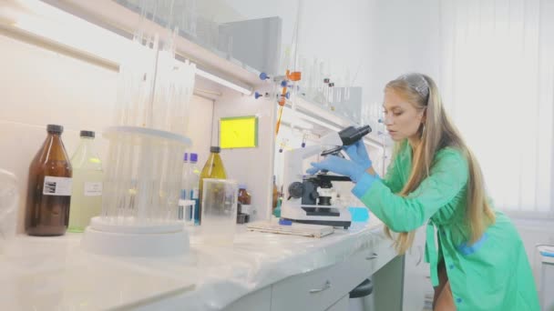 The girl researcher looks in a microsom. Young girl virologist looks through a microscope — Stock Video
