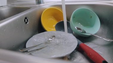 Mutfakta rutin işler. Kirli bulaşıklar lavaboda. Musluk suyu kirli tabaklara dökülür. Bulaşık yıkama işlemi. Ev ödevi