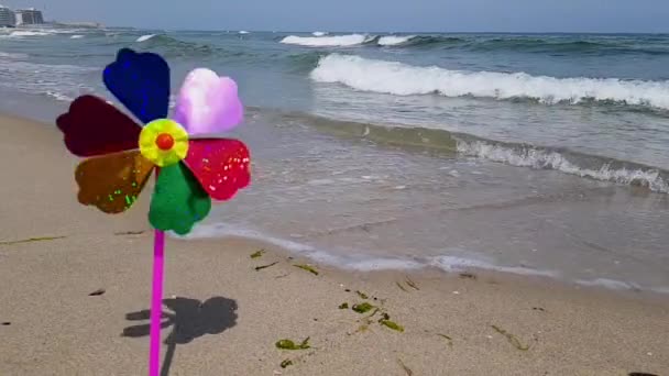 Un moulin à vent pour enfants coloré tourne à partir du vent sur le bord de la mer. Moulin à vent pour enfants sur la mer. Un moulin à vent pour enfants dans le vent — Video