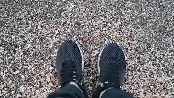 Zapatillas negras en la playa del mar. Las olas casi alcanzan las zapatillas negras en la playa. Piernas de un hombre en zapatillas en la orilla del mar — Vídeos de Stock