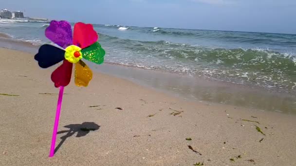 Barnväderkvarn på havet. En väderkvarn för barn i vinden, en färgad väderkvarn för barn snurrar från vinden på stranden. — Stockvideo