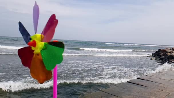 O moară de vânt pentru copii în vânt, o moară de vânt colorată pentru copii se rotește de la vântul de pe țărmul mării. Moara de vânt pentru copii pe mare — Videoclip de stoc