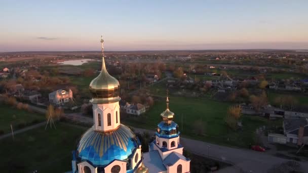 Orthodoxe kerk in het dorp bij zonsondergang. Kerk in de buurt van de rivier vanuit de lucht — Stockvideo