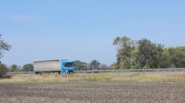Kamyon otoyolda gidiyor. Kamyon tarlaların ve ağaçların etrafındaki otoyolda ilerliyor.