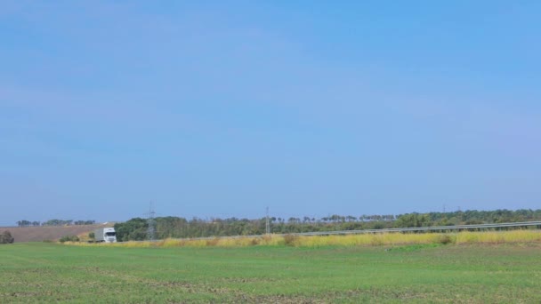 Ciężarówka jeździ płaską, nowoczesną drogą poza miastem. Ciężarówka jedzie wzdłuż drogi w słoneczny dzień. — Wideo stockowe