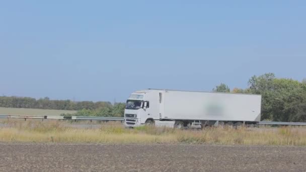 Ciężarówka jeździ płaską, nowoczesną drogą poza miastem. Ciężarówka jedzie wzdłuż drogi w słoneczny dzień. — Wideo stockowe
