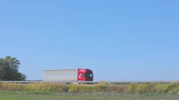 Ein LKW mit rotem Führerhaus fährt die Autobahn entlang. Der LKW fährt die Straße entlang. Lieferung von Waren per LKW — Stockvideo