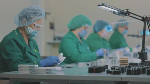 Жінки спакують таблетки в пакеті. Заводські робітники носять маски. робота під час пандемії — стокове відео