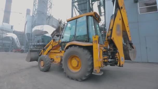 Žlutý traktor projíždí územím závodu. Žlutý traktor v pohybu. Traktor projíždí továrnou. — Stock video