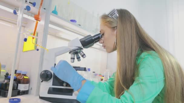 Giovane virologo ragazza guarda attraverso un microscopio. Il ricercatore di ragazza guarda in un microsom. — Video Stock