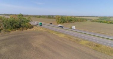 Bir kargo kamyonu otoyol boyunca gidiyor. İnsansız hava aracı görüntüsü. Vagon, tarlaların üst manzarası arasında virajlı bir yolda ilerliyor.