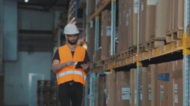 Büyük bir fabrikanın depo müdürü. Bir depoda elinde tablet olan bir müdür malları kontrol ediyor.