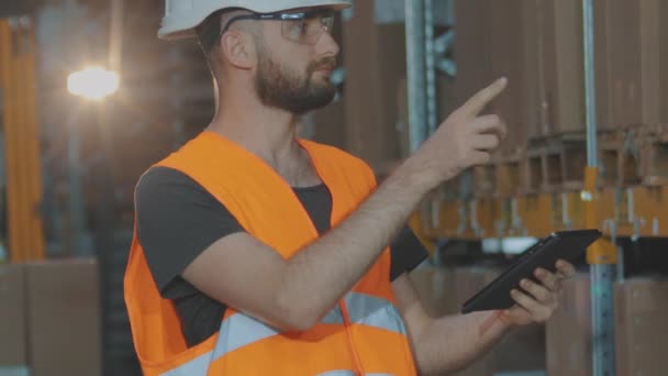 El gerente del almacén inspecciona el almacén. Un hombre en un almacén moderno. Trabajador en un casco en un almacén — Vídeos de Stock