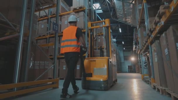 Ein Arbeiter transportiert Kisten auf einem hydraulischen Gabelstapler. Arbeitsprozess im Lager. Mann transportiert Waren in einer Lagerhalle — Stockvideo