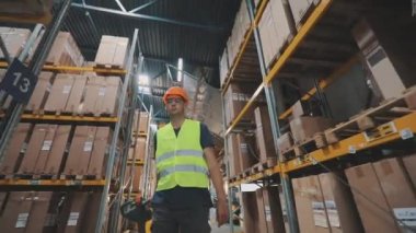 Depoda çalışan bir işçi bir Palet Yük Kamyonu taşıyor. Depoda forklift kullanan bir işçi. İşçi depoda yürüyor.