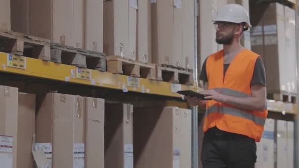 Il direttore del magazzino ispeziona il magazzino. Un uomo in un magazzino moderno. Lavoratore in un casco in un magazzino — Video Stock