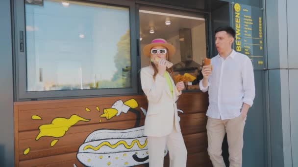 Fata cu un tip care mănâncă hot dog. Cuplu tânăr elegant care mănâncă hot dog — Videoclip de stoc