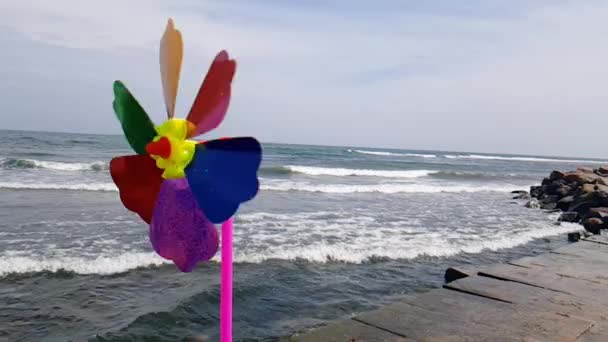 Um moinho de vento colorido infantil está girando na praia. Moinho de vento infantil no mar. Moinho de vento infantil — Vídeo de Stock