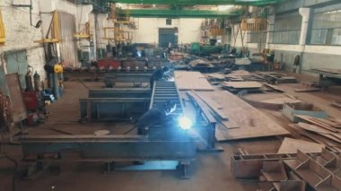 Metal yapıların montajı için bir fabrika. Metal montaj atölyesinde kaynakçı. Metal yapıların montajı için atölye boyunca bir açıklık.
